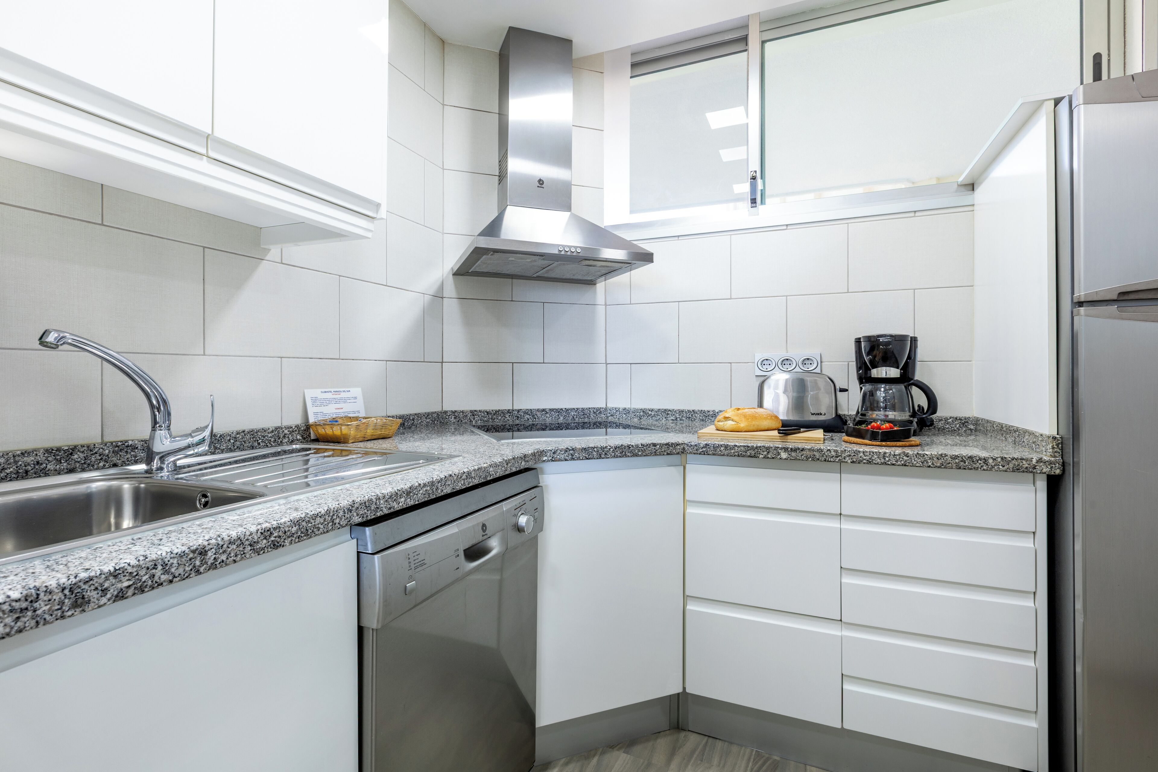 Una cucina moderna con lavastoviglie in acciaio inossidabile, forno integrato e macchina del caffè sul piano di lavoro.