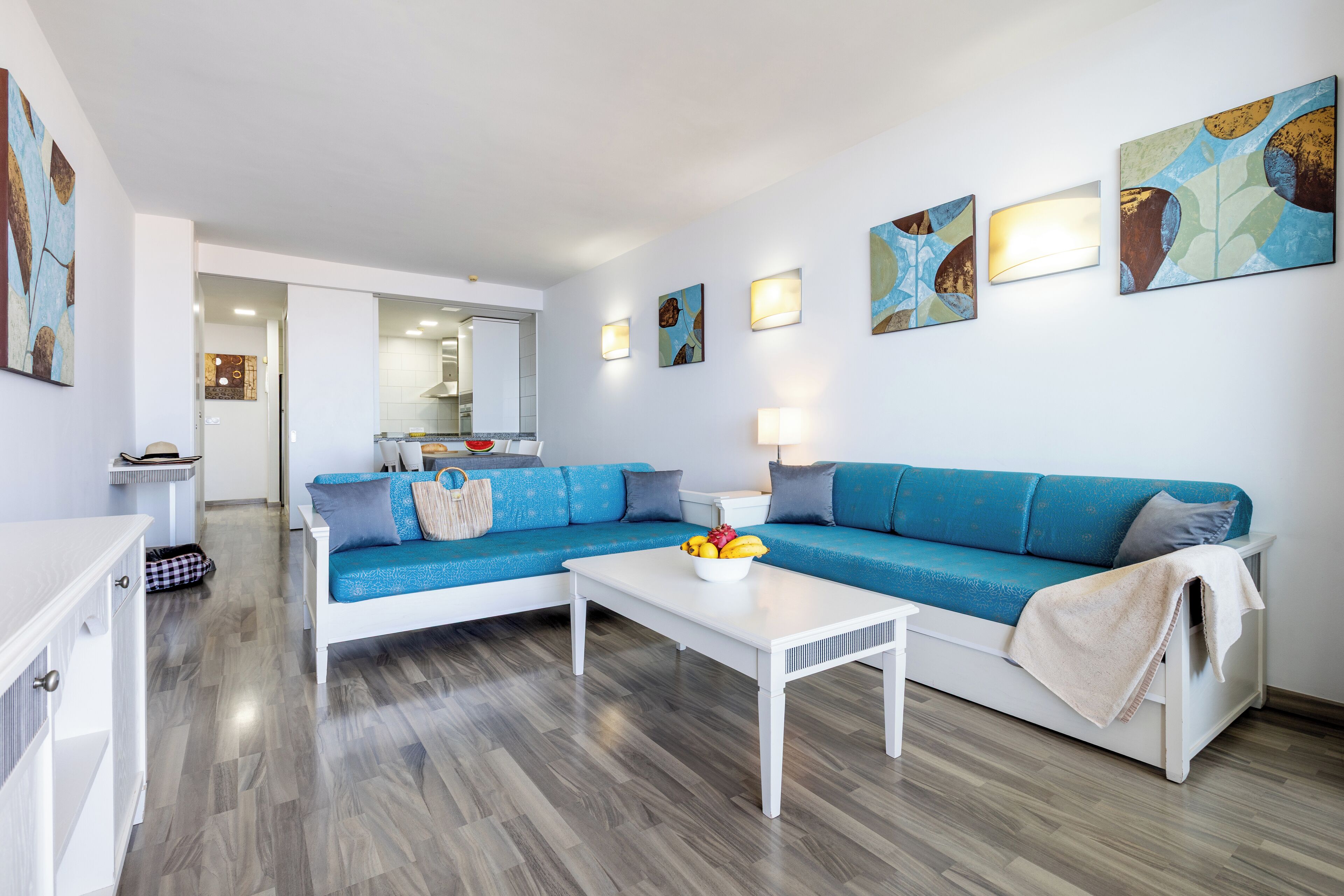 Una sala de estar moderna con un sofá azul, una mesa de centro blanca y obras de arte en las paredes.