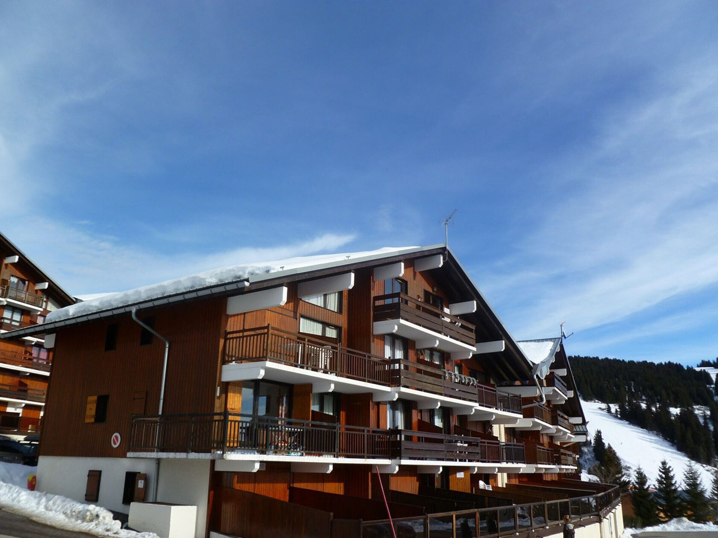 A multi-story wooden building with balconies, likely a hotel or resort, set against a snowy mountain backdrop.