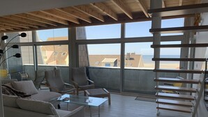 Un vaste balcon offrant une vue sur la plage, aménagé avec un canapé, des fauteuils et une table basse en verre.