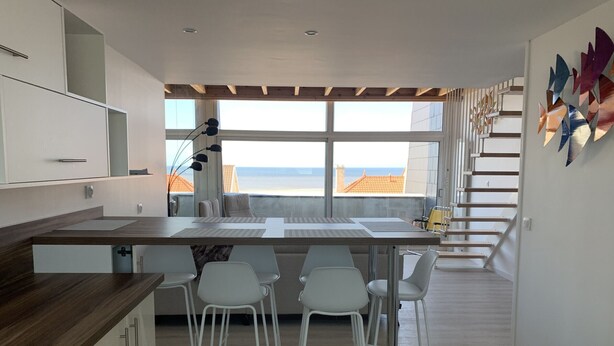 Une cuisine moderne dotée d’un grand îlot central, de tabourets de bar blancs et offrant une vue sur l’océan.
