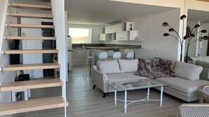 Un intérieur moderne comprenant un escalier, un espace de vie avec un canapé, une table basse en verre et un coin cuisine.