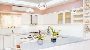 A modern kitchen with white cabinets, a central island with plants, and pendant lighting.