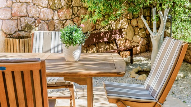 A wooden table with striped cushions, a potted plant, and a stone wall in the background.