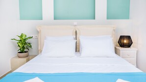 A neatly made bed with white linens, a bedside plant, and a nightstand with a lamp.