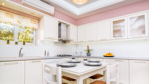 A modern kitchen with white cabinets, a dining table set for four, and a window with plants.