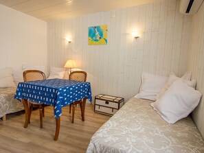 Quarto com duas camas, uma mesa com toalha azul, duas cadeiras, um abajur e um quadro na parede.