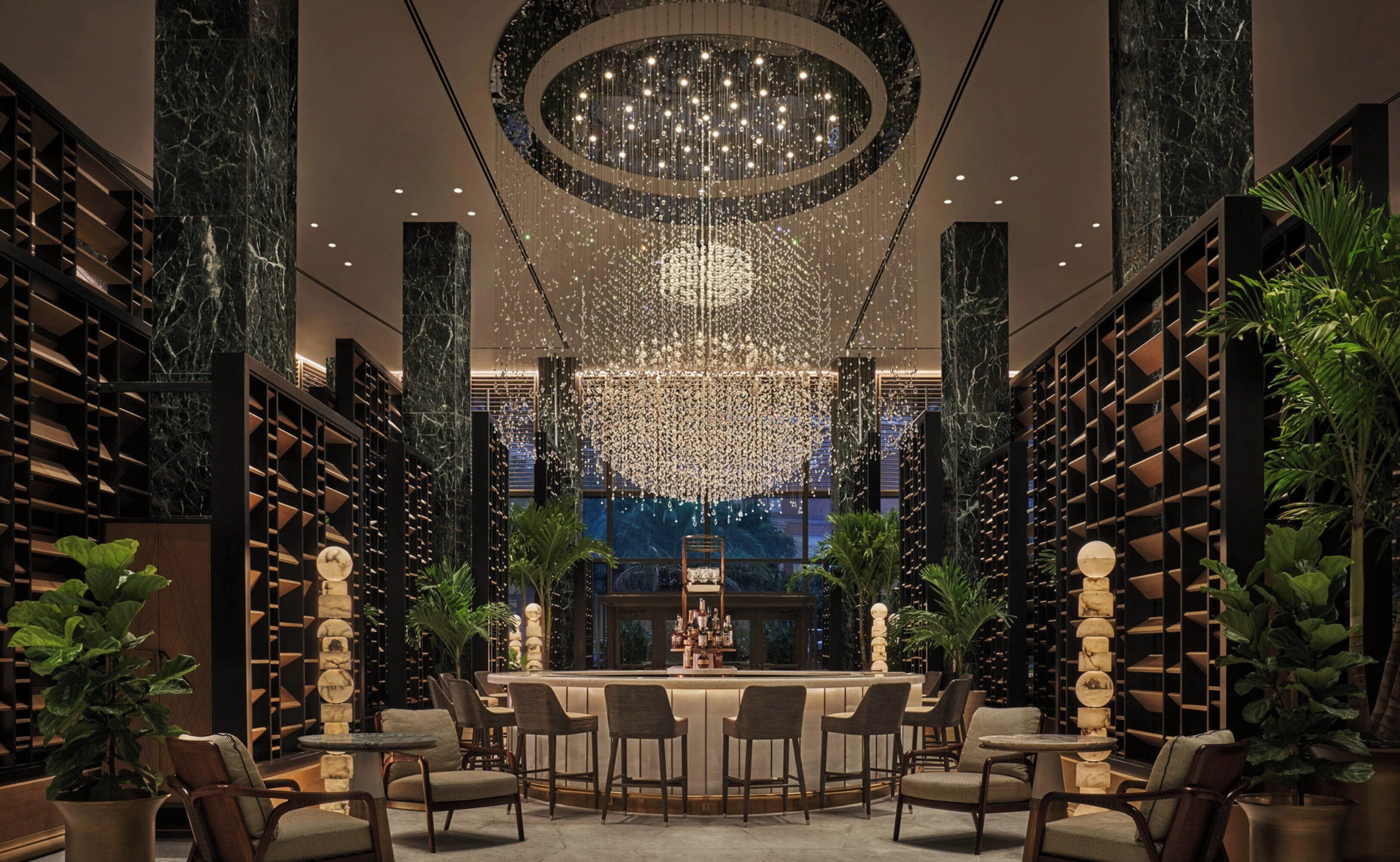 A bar area with a circular chandelier, marble columns, and bookshelves.