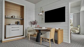 A modern living room with a dining area, a flat-screen TV mounted on the wall, a wooden cabinet with kitchenware, and a round table with chairs.