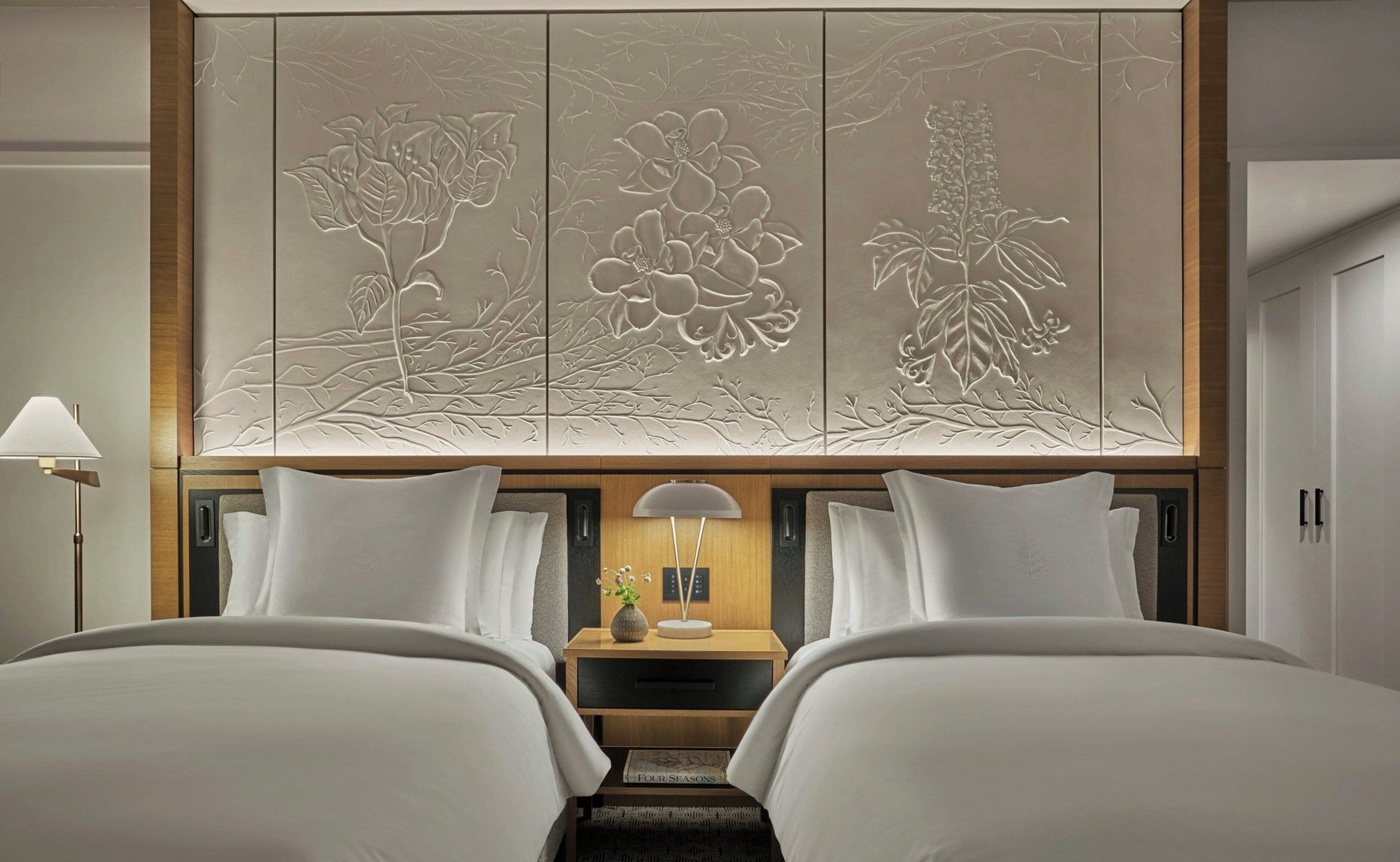 A hotel room with two beds, a nightstand with a lamp, and a decorative panel with floral designs.