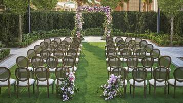 A wedding ceremony setup with rows of wicker chairs and a floral archway.