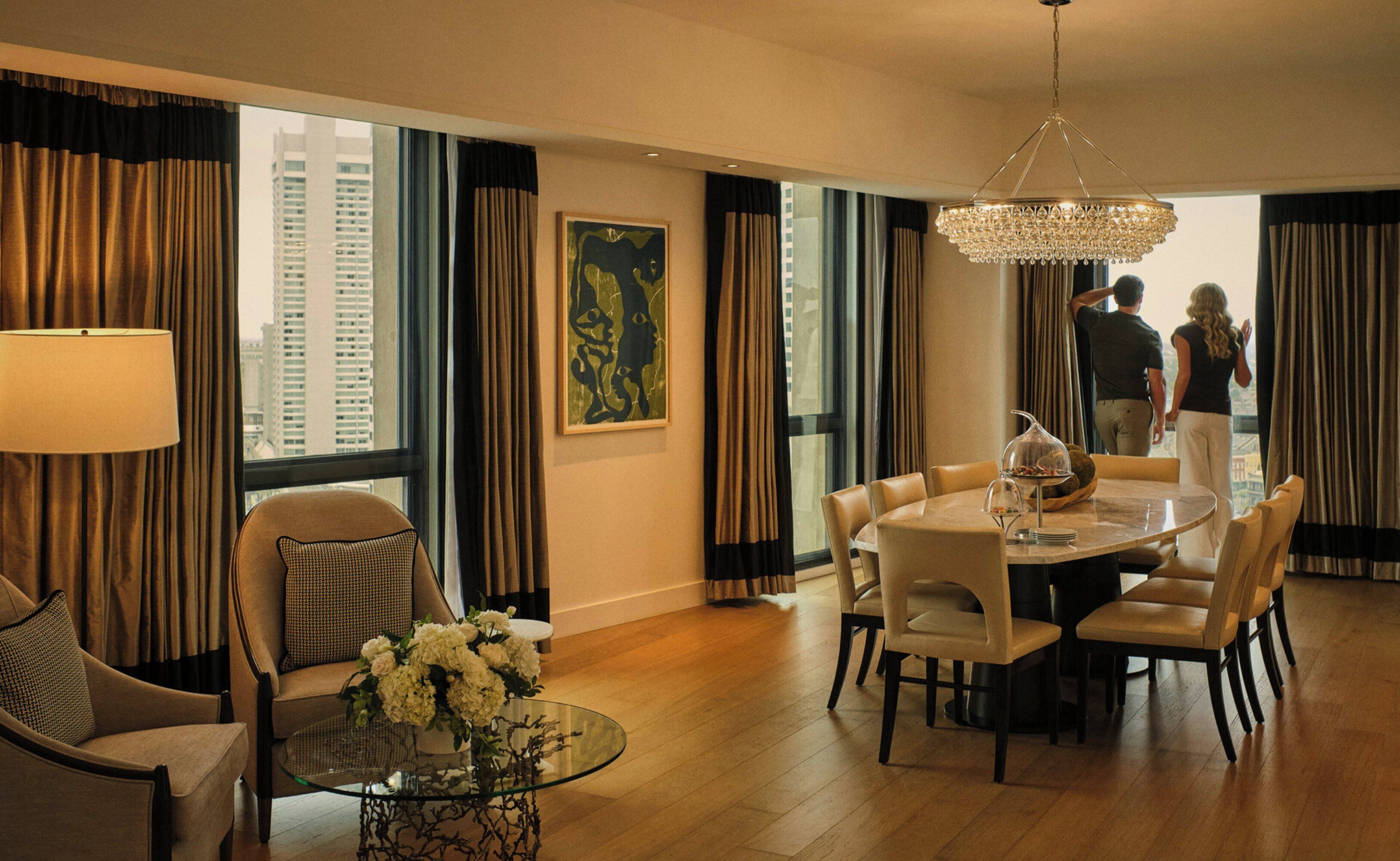 Uma área de refeições de hotel com uma mesa redonda, cadeiras, uma mesa de centro de vidro e um candelabro.