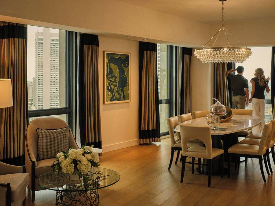 Uma área de refeições de hotel com uma mesa redonda, cadeiras, uma mesa de centro de vidro e um candelabro.
