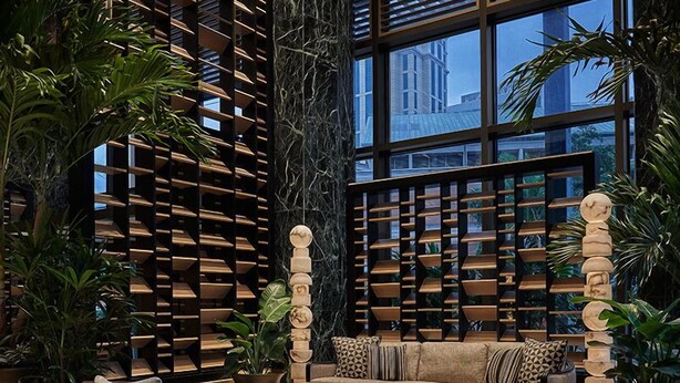 A modern lounge area with a sofa, chairs, and a coffee table, surrounded by bookshelves and potted plants.