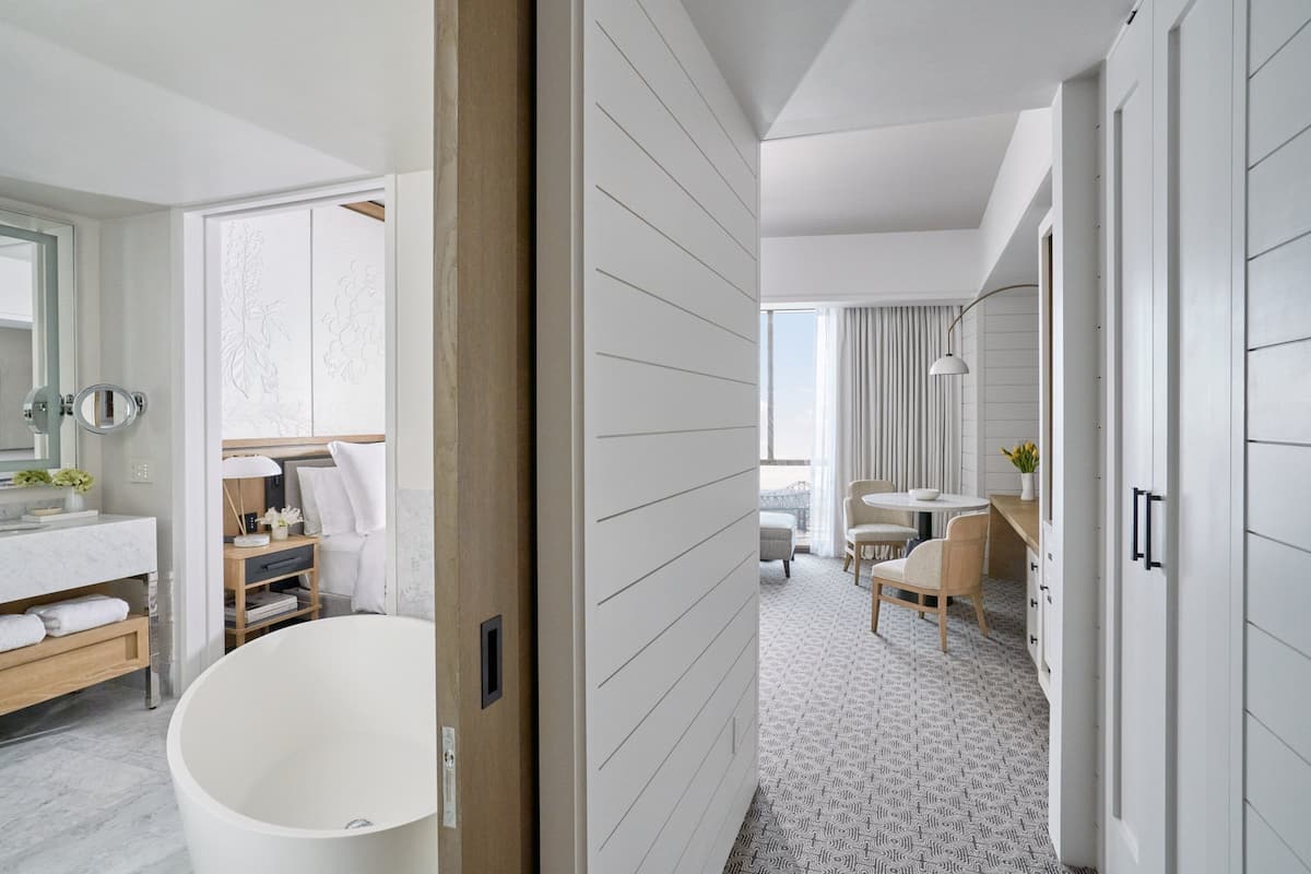 Ein modernes Hotelzimmer mit einer großen Badewanne, einem Schminktisch mit Spiegel und einem Essbereich mit Tisch und Stühlen.