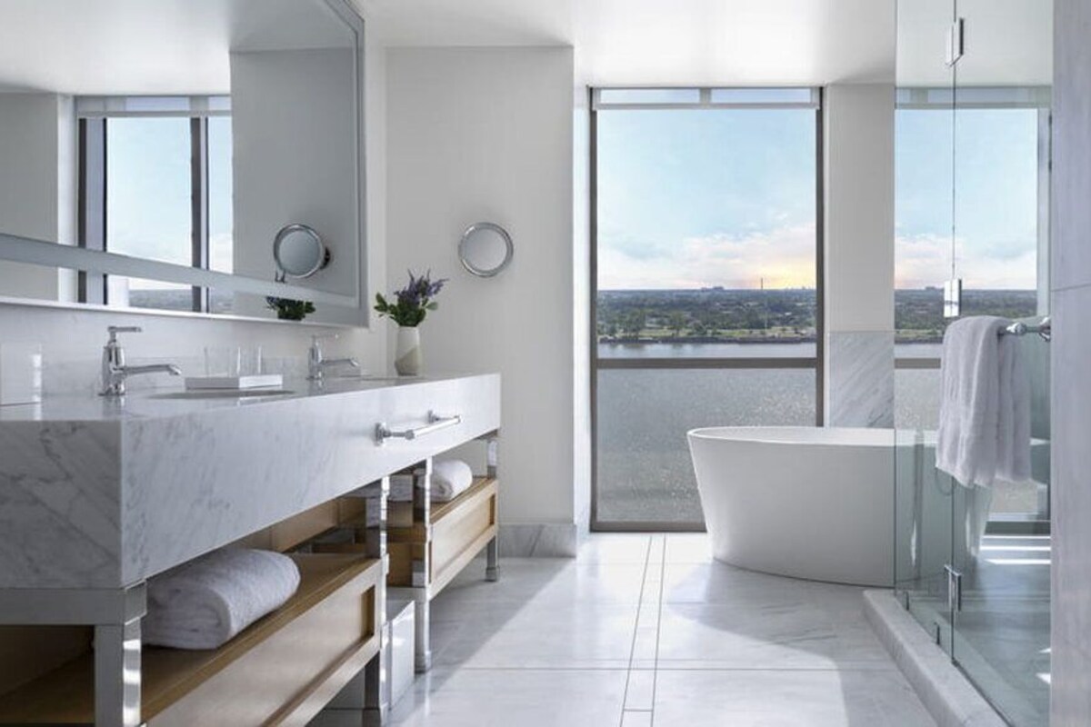 A modern bathroom with a large bathtub, a vanity with a mirror, and a view of a cityscape through large windows.