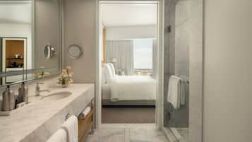A hotel bathroom with a marble sink, a large mirror, a shower area, and a view of the city through the window.