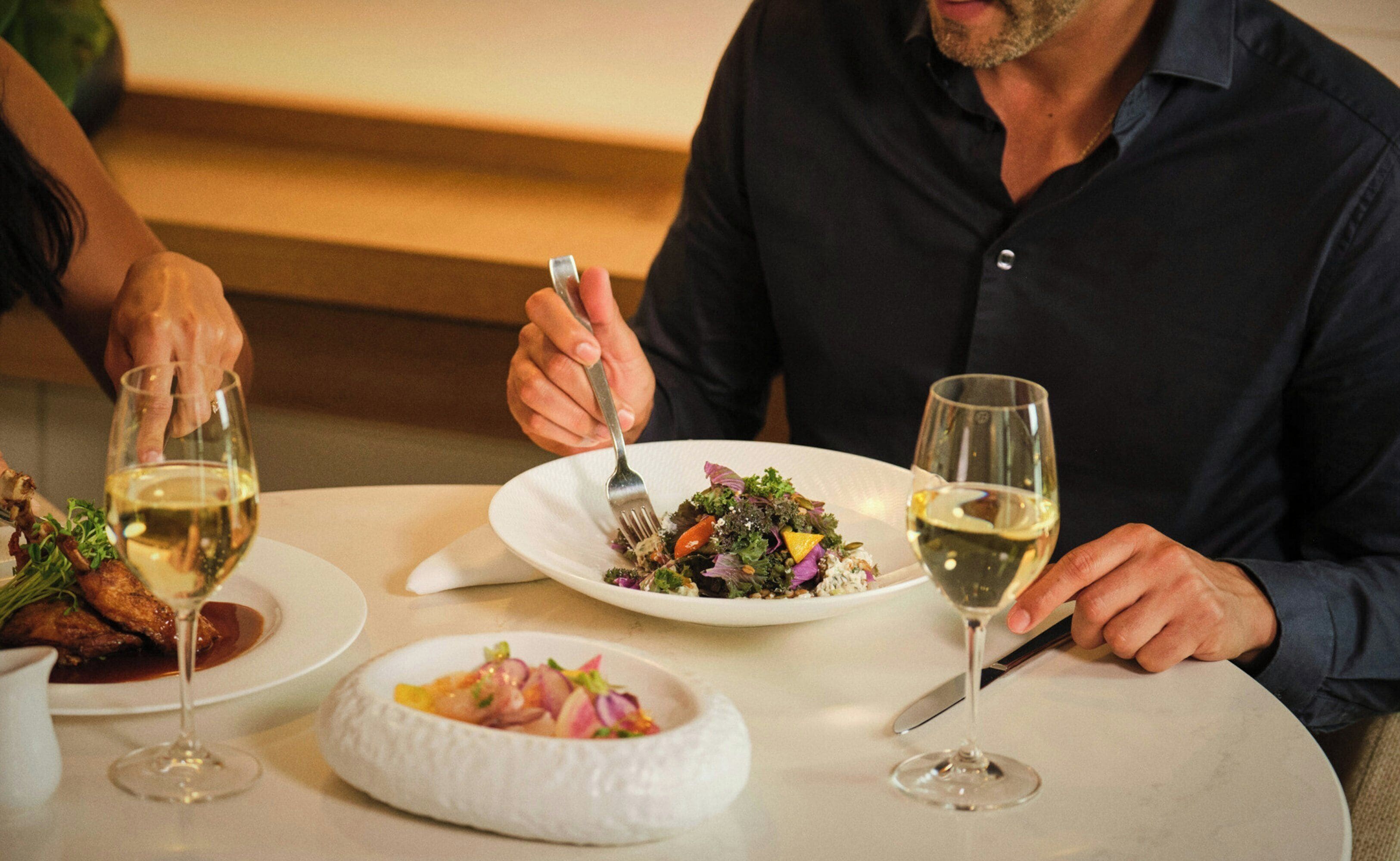 A dining table with plates of food, wine glasses, and a fork.