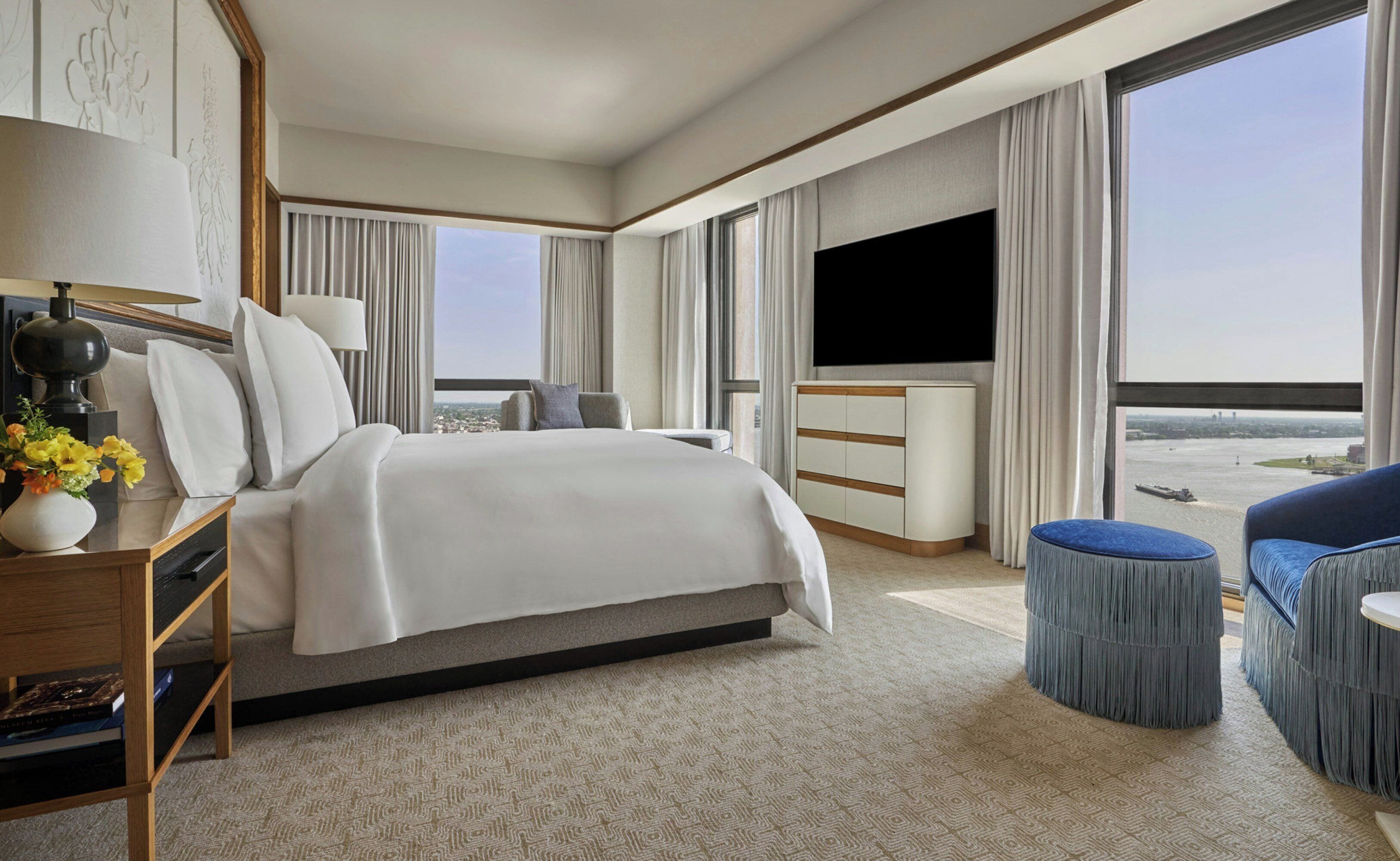A hotel room with a large bed, a flat-screen TV, a desk with a lamp, and a view of the city.