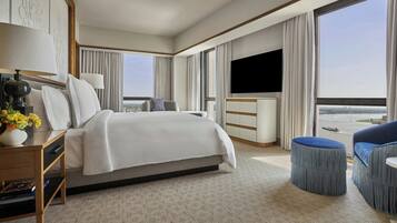 A hotel room with a large bed, a flat-screen TV, a desk with a lamp, and a view of the city.