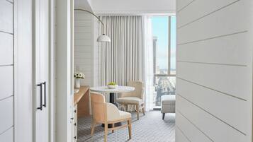 Habitación de hotel moderna con balcón, una mesa redonda, dos sillas, un florero con flores y vistas a la ciudad.