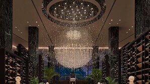 A luxurious lobby with a central bar, marble columns, and a chandelier.
