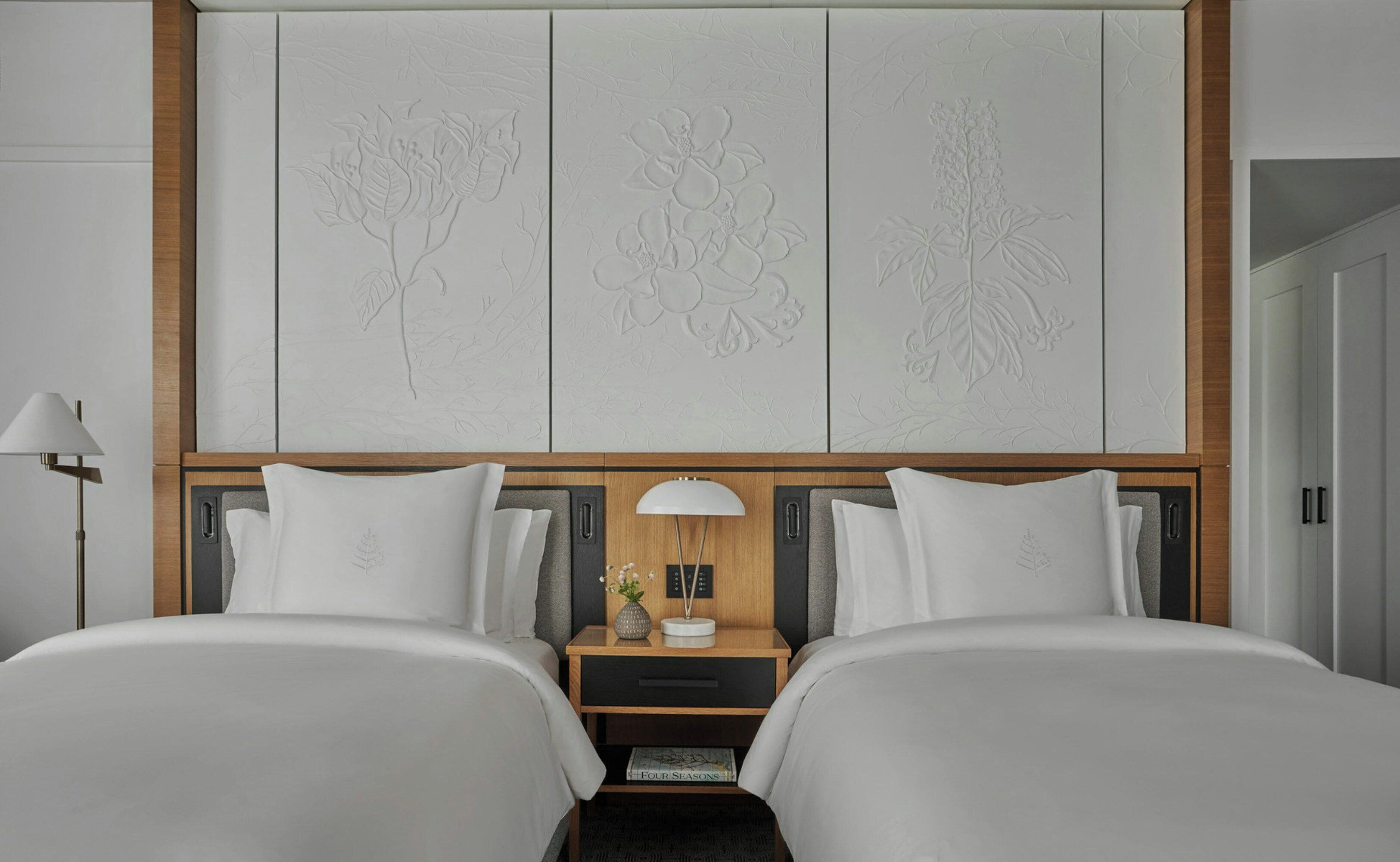 A hotel room with two beds, a nightstand with a lamp, a decorative wall panel, and a door.