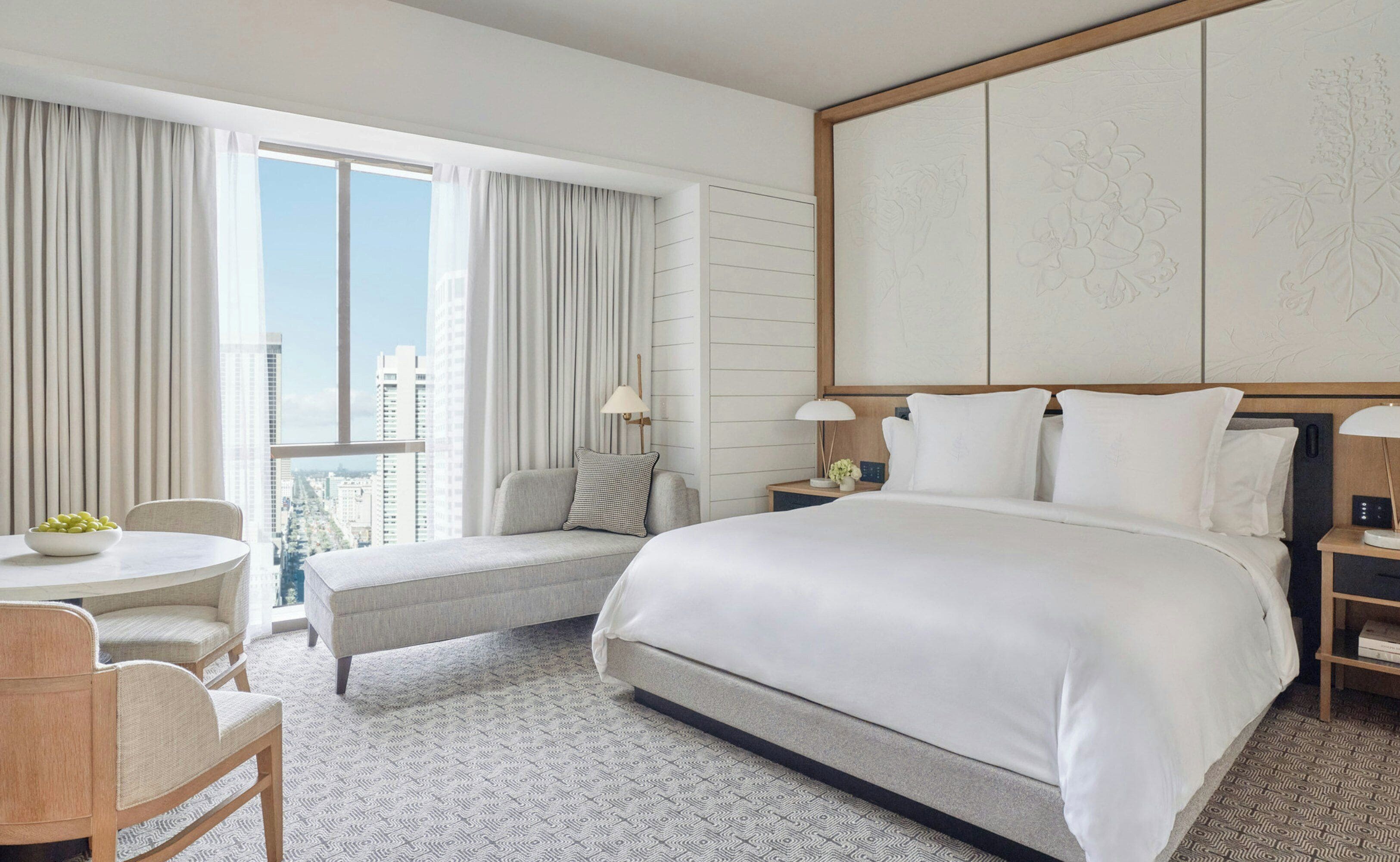 A hotel room with a large bed, a seating area with a table, and a view of the cityscape.