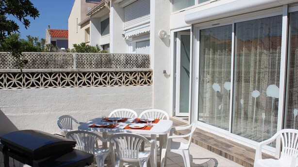 A patio with a table and chairs, a grill, and a sliding glass door with a mesh screen.
