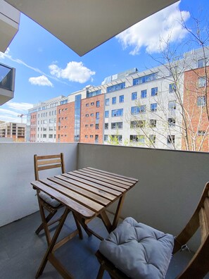 A balcony with a wooden table and chairs, a cushioned bench, and a view of multi-story buildings.
