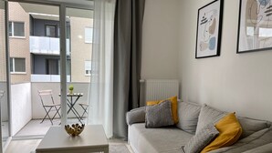 Uma sala de estar moderna com um sofá cinzento, uma mesa de centro branca e uma varanda com uma cadeira e uma mesinha.
