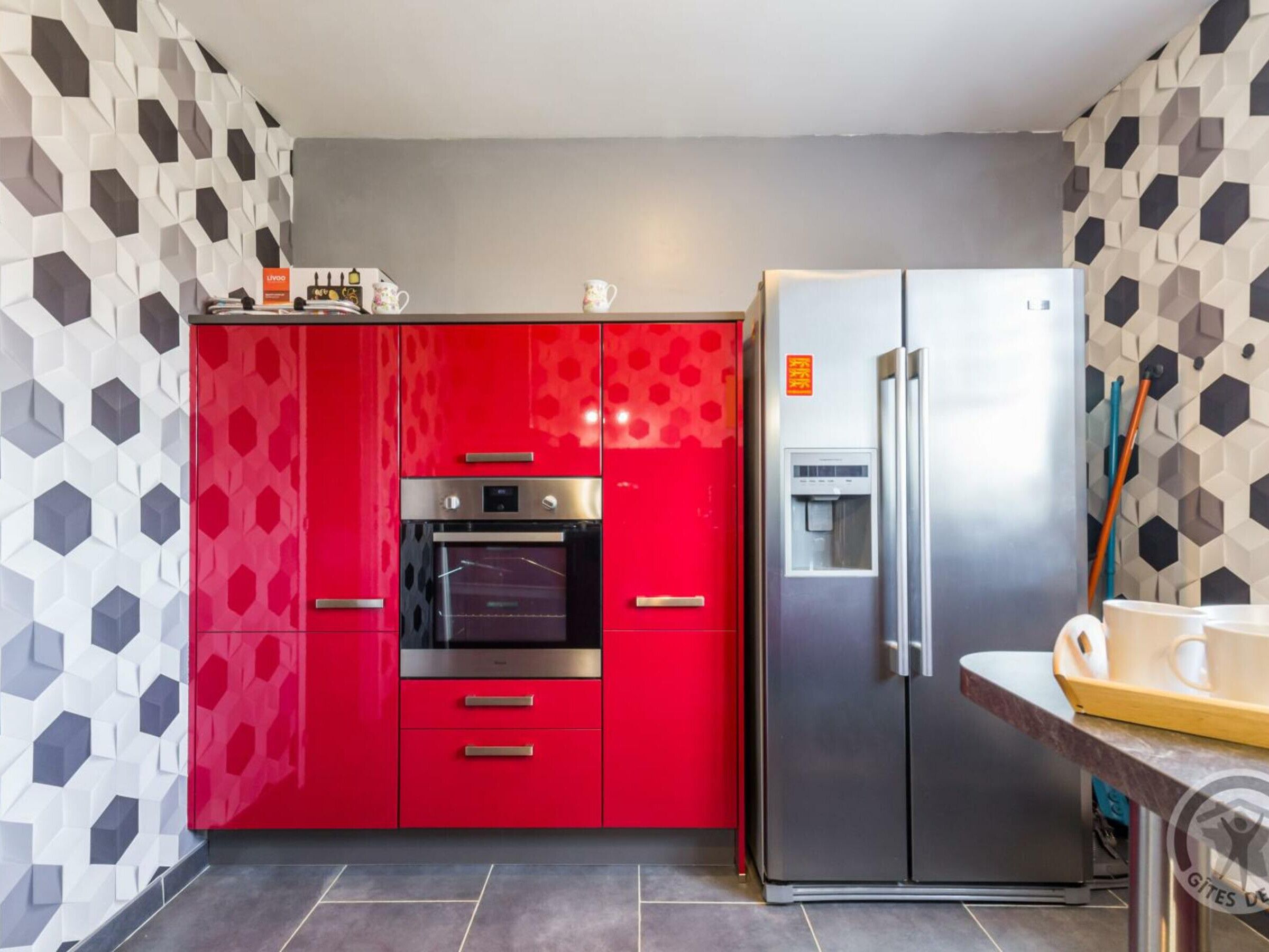 A modern kitchen with red cabinets, a built-in oven, and a stainless steel refrigerator.