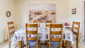 A dining area with a table set for four, surrounded by wooden chairs. A large landscape painting is on the wall above the table. - Single-level house with terrace, enclosed garden and pets allowed (Anneville-en-Saire)