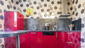 A modern kitchen with red cabinets, a black countertop, and a hexagonal patterned wall. - Single-level house with terrace, enclosed garden and pets allowed (Anneville-en-Saire)