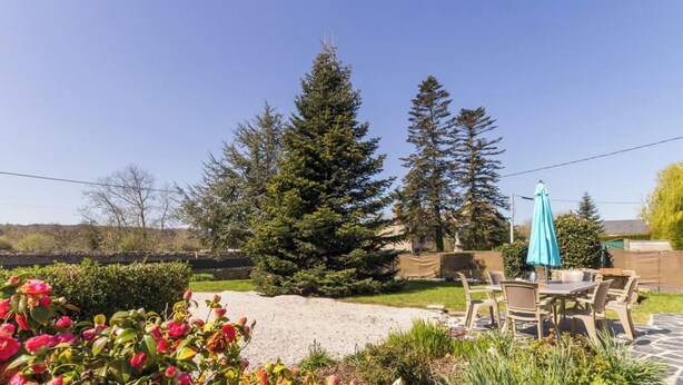 A patio area with a table and chairs, surrounded by a garden with various plants and a large coniferous tree. - Single-level house with terrace, enclosed garden and pets allowed (Anneville-en-Saire)