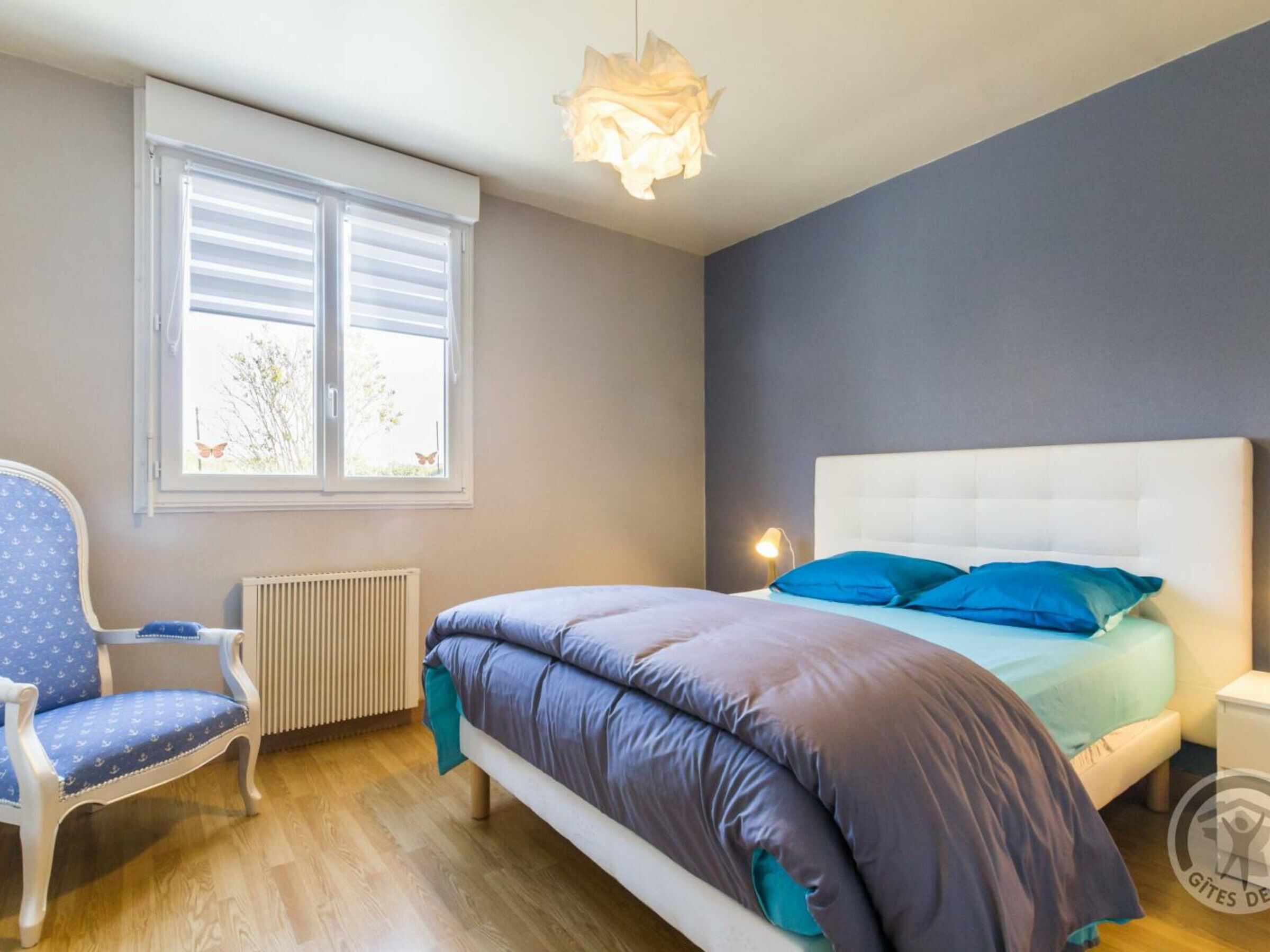 Een slaapkamer met een bed, een stoel, een radiator en een raam met zonwering.