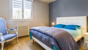 A bedroom with a bed, a chair, a radiator, and a window with blinds. - Single-level house with terrace, enclosed garden and pets allowed (Anneville-en-Saire)