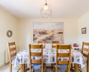 Un comedor con una mesa dispuesta para cuatro personas, rodeada de sillas de madera. Un cuadro grande de paisaje adorna la pared sobre la mesa.