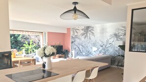 Een moderne keuken met een houten aanrecht, witte stoelen en een eettafel. Er is een groot raam met uitzicht op groen.