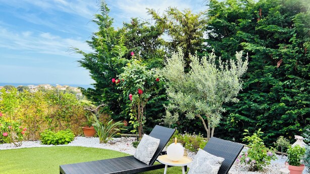 Een tuin met twee zwarte loungestoelen, een bijzettafeltje en diverse planten en bomen.