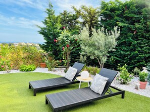 A garden with two black lounge chairs, a small table, and a variety of plants and trees. - Villa Individuelle sur la French Riviera (Saint-Laurent-du-Var)
