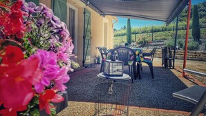 An outdoor patio with a table and chairs, a pergola providing shade, and a garden with flowers and plants.
