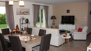 A modern living room with a dining area, white sofas, a TV, and a fireplace.