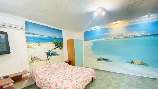 Un dormitorio con una cama, un escritorio y un mural en la pared con una escena de playa.
