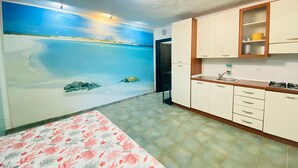 Un dormitorio con cama, un cuadro de una escena de playa, kitchenette y baño.