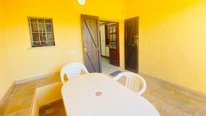 Una habitación con una pared amarilla, una puerta de madera, una ventana con barrotes y una mesa con sillas.