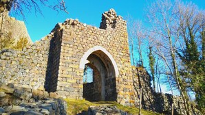 Une ruine de pierre avec une entrée en arc de cercle, entourée d’arbres et surplombant un ciel bleu clair.