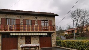 Un bâtiment en pierre de deux étages, doté d’un balcon, d’un banc en bois et d’une table recouverte d’une nappe blanche.