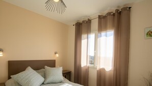 Un dormitorio con cama, dos lámparas de noche, una ventana con cortinas y una lámpara de pared.