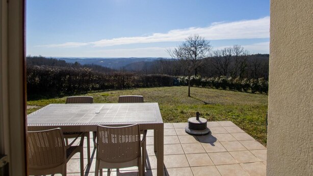 Un patio exterior con mesa y sillas, un pozo de fuego y vistas a colinas y árboles a lo lejos.